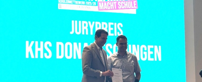 Herr Bader steht neben Andreas Jung vor einer Leinwand und empfängt die Auszeichnung